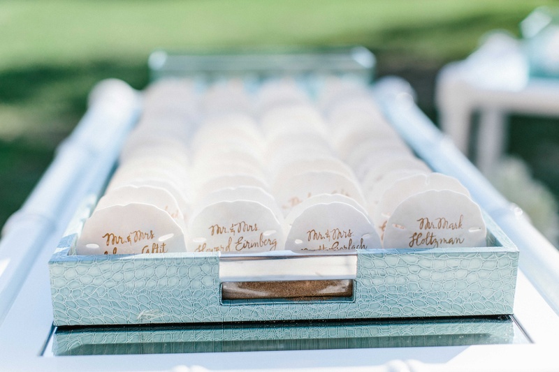 Calligraphy on Seashell Escort Cards
Photography: Braedon Photography
Read More:
http://www.insideweddings.com/weddings/orthodox-jewish-wedding-with-outdoor-ceremony-inspired-by-the-sea/812/ Wedding place cards for oceanfront ceremony seashell place cards in light blue tray on bar cart