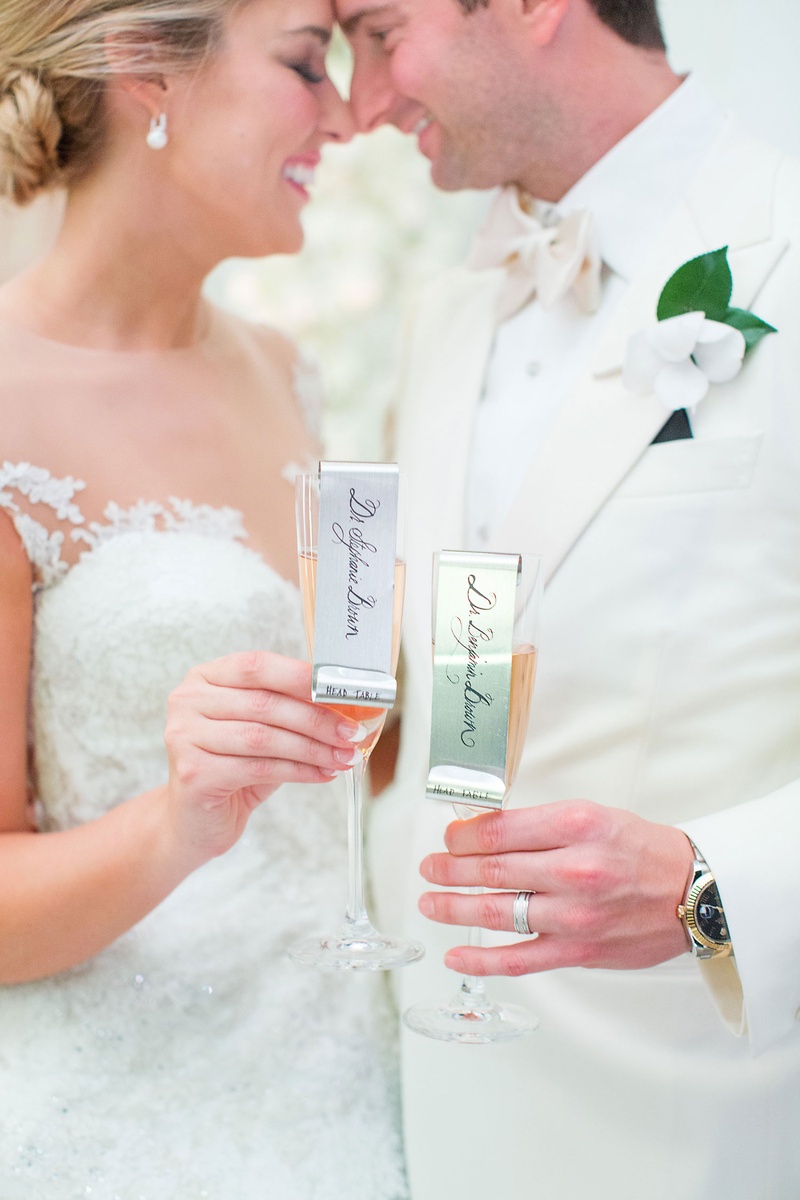 Metallic Ribbon on Champagne Glass
Photography: Sarah Kate, Photographer
Read More:
http://www.insideweddings.com/weddings/outdoor-fall-ceremony-opulent-tented-reception-in-dallas-texas/1022/ Bride and groom touch noses foreheads while holding rose champagne with metal name tags escort cards
