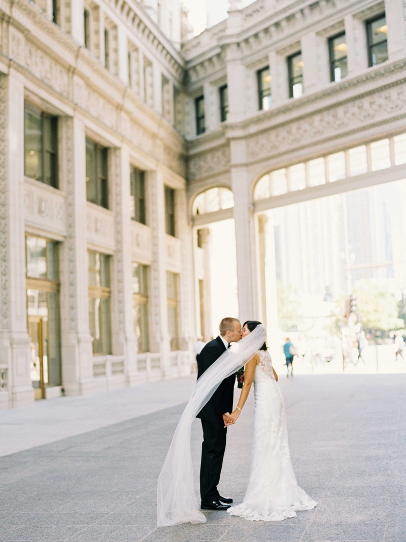 Couple Kisses as Veil Flies in Wind
Photography: Amanda Sudimack for Artisan Events
Read More:
http://www.insideweddings.com/weddings/customized-chicago-wedding-with-pink-blush-marsala-color-palette/911/ Bride in lace wedding dress with long veil kisses groom in Chicago courtyard tuxedo bow tie