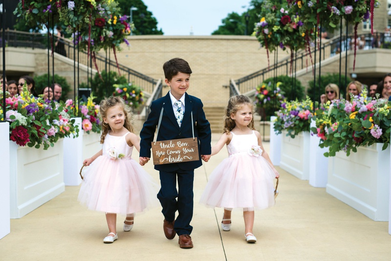 Ring Bearer Holding Flower Girls' Hands
Photography: Kent Drake Photography
Read More:
http://www.insideweddings.com/weddings/bright-and-colorful-wedding-palette-with-ceremony-overlooking-lake/1315/ ring bearer with wooden sign around neck holds hands with two flower girls in blush dresses