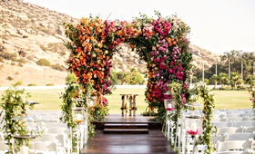 Colorful Ceremony Chuppah at Ranch
Photography: Laurie Bailey Photography
Read More:
http://www.insideweddings.com/weddings/outdoor-jewish-ceremony-reception-with-colorful-bohemian-decor/1330/ outdoor wedding reception dark wood aisle with white chairs greenery pink orange yellow flowers