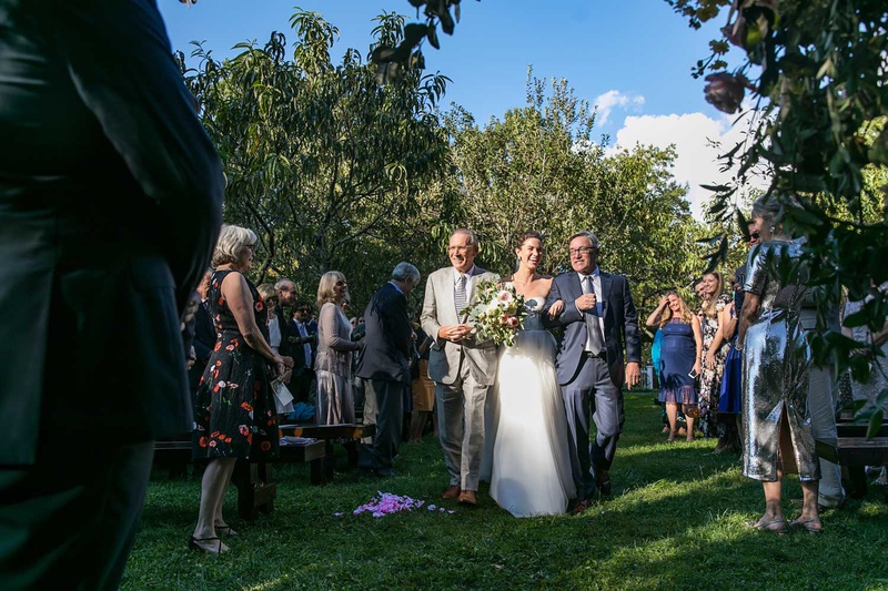 Bride Walking with Father %26 Stepfather
Photography: Vue Photography
Read More:
http://www.insideweddings.com/weddings/destination-rustic-fall-wedding-at-a-farm-in-north-carolina/1202/ bride walking down grass aisle with dad and stepdad in grey suits guests standing