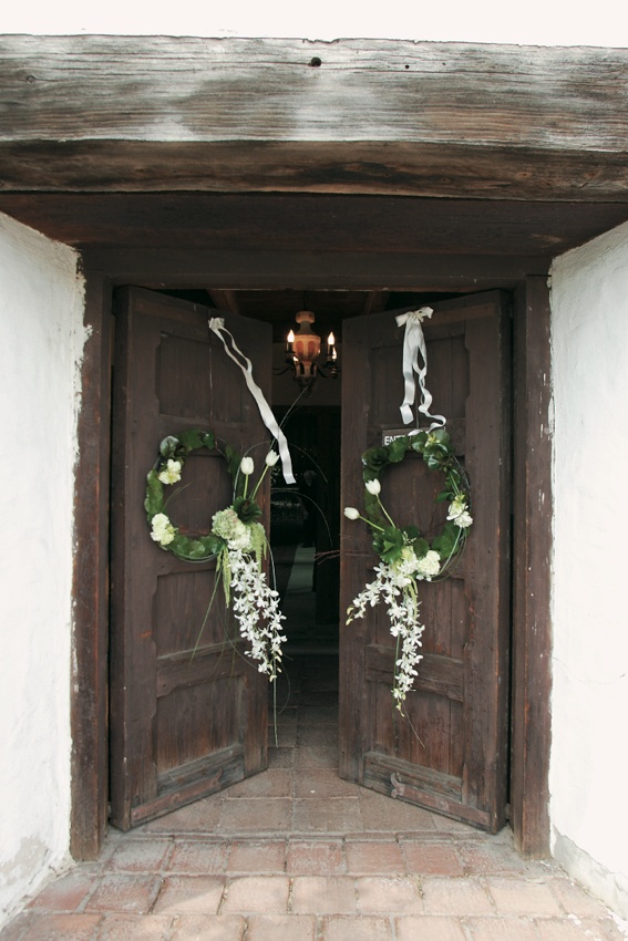 Ceremony Decor
Photography: Sherman Chu Photographer
Read More:
http://www.insideweddings.com/weddings/elegant-garden-style-vineyard-wedding-in-sonoma-california/205/ Church doors decorated with white ribbons and green wreaths with white flowers