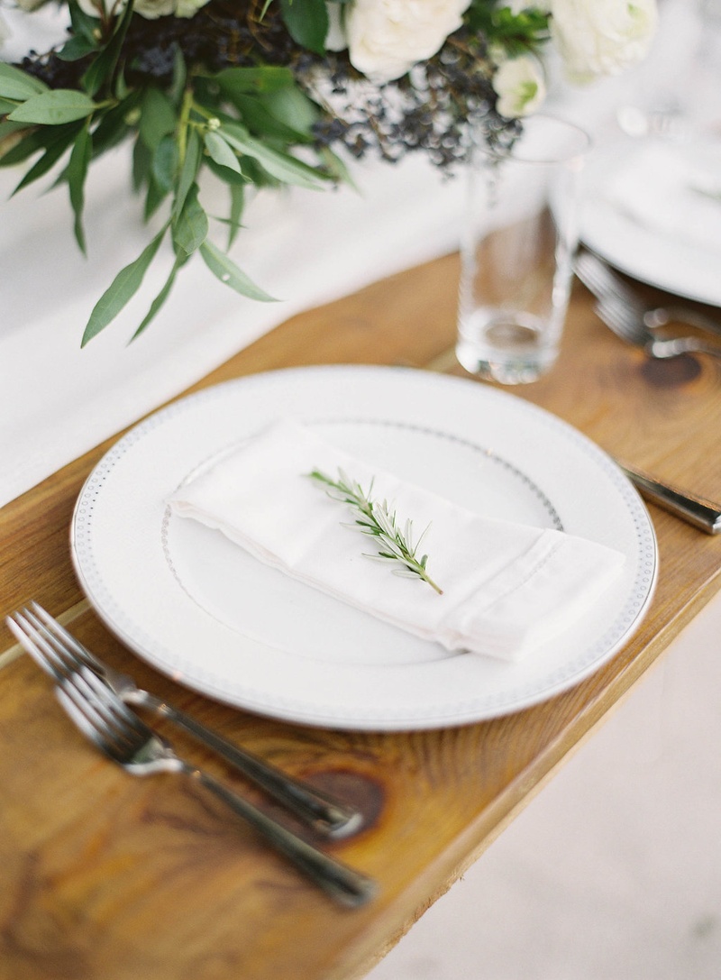 Fresh Herb Sprig on Plate
Photography: Jacqui Cole Photography
Read More:
http://www.insideweddings.com/weddings/alfresco-ceremony-dinner-reception-at-an-elegant-villa-in-miami/1020/ White china plate on wood table sprig of fresh rosemary on napkin on plate silver flatware