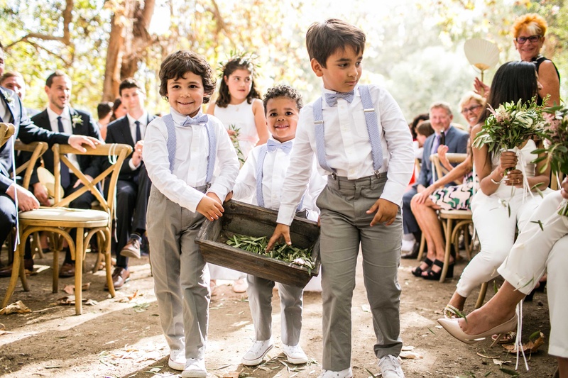 Ring Bearers Tossing Olive Leaves
Photography: Samuel Lippke Studios
Read More:
http://www.insideweddings.com/weddings/a-rustic-camp-themed-outdoor-wedding/908/ Boy ring bearers in grey pants and blue suspenders and bow ties tossing olive sprig leaves on aisle