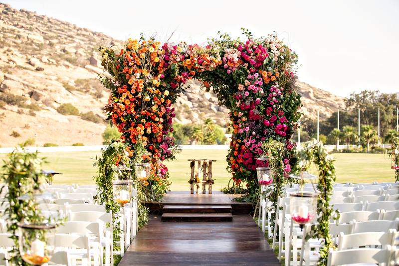 Colorful Ceremony Chuppah at Ranch
Photography: Laurie Bailey Photography
Read More:
http://www.insideweddings.com/weddings/outdoor-jewish-ceremony-reception-with-colorful-bohemian-decor/1330/ outdoor wedding reception dark wood aisle with white chairs greenery pink orange yellow flowers