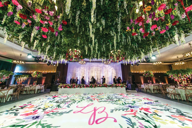 Vibrant Dance Floor with Ceiling Installation
Photography: Kent Drake Photography
Read More:
http://www.insideweddings.com/weddings/bright-and-colorful-wedding-palette-with-ceremony-overlooking-lake/1315/ white dance floor painted with floral watercolor and pink initials, lush floral ceiling installation