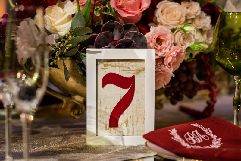 Burgundy Table Number in Frame
Photography: Kent Drake Photography
Read More:
http://www.insideweddings.com/weddings/an-event-planners-wedding-at-a-museum-by-sue-the-tyrannosaurus-rex/955/ White frame with gold background and burgundy table number next to centerpiece with roses succulents
