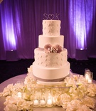 Purple Sugar Flower Cake
Photography: Next Exit Photography
Read More:
http://www.insideweddings.com/weddings/alfresco-interfaith-ceremony-ballroom-reception-in-santa-monica/963/ Four layer white wedding cake with heart design and purple sugar flower ribbon white flowers lucite