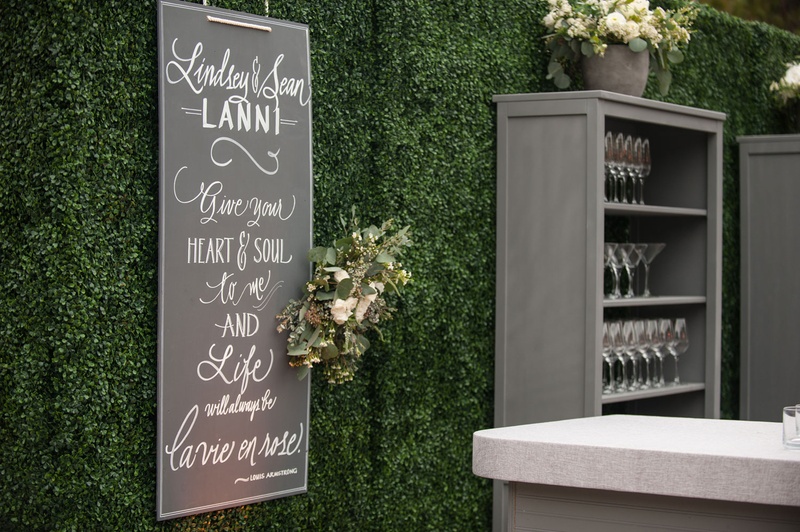 Hedge Wall with Signage at Wedding
Photography: Triple Cord Photography
Read More:
http://www.insideweddings.com/weddings/destination-wedding-with-outdoor-reception-lavish-after-party/982/ Outdoor wedding green boxwood hedge wall chalkboard sign Louis Armstrong quote grey bookshelf bar