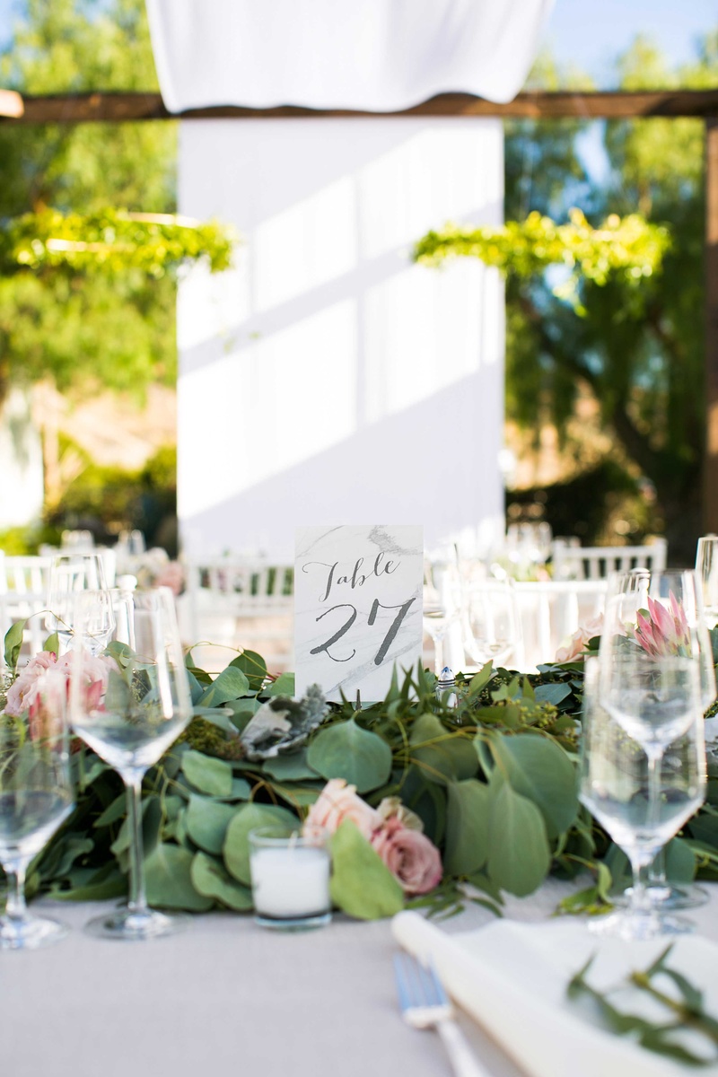 Table Number Surrounded by Foliage
Photography: Callaway Gable
Read More:
http://www.insideweddings.com/weddings/alfresco-summer-wedding-with-lush-foliage-accents-in-california/805/ table number in gray calligraphy surrounded by foliage with blush flowers on white table linen
