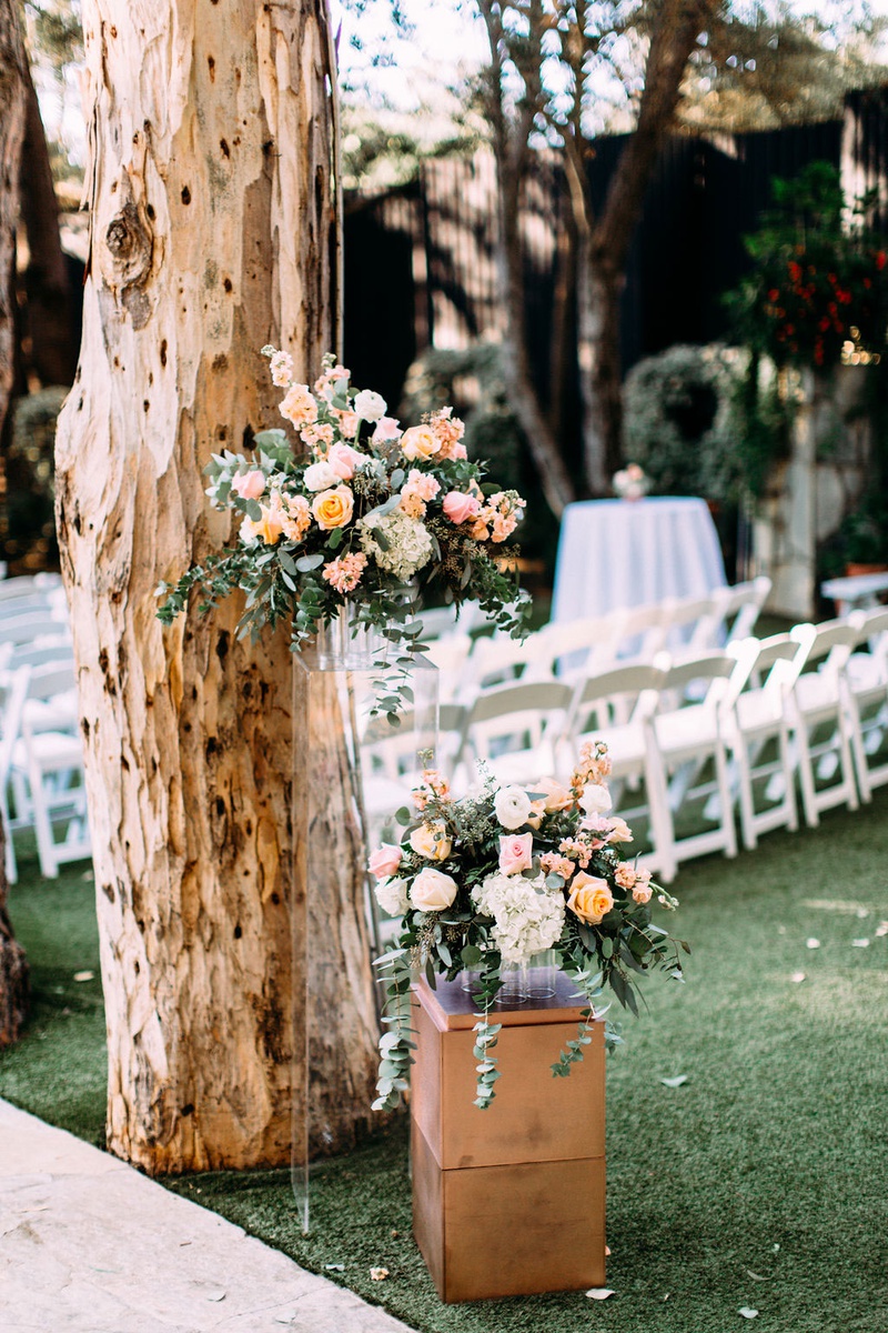 Ceremony Florals on Acrylic Riser
Photography: Ashley Paige Photography
Read More:
http://www.insideweddings.com/weddings/elegant-outdoor-fall-wedding-at-a-rustic-chic-venue-in-malibu/1244/ wedding ceremony tall tree with lucite riser holding peach pink flower arrangement greenery