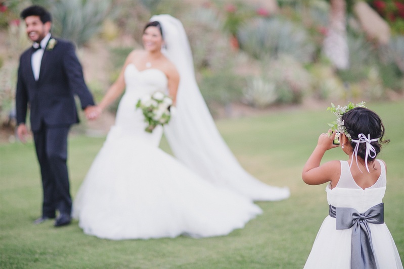 Bow-Embellished Dress
Photography: Jasmine Star Photography
Read More:
http://www.insideweddings.com/weddings/spanish-style-ceremony-outdoor-ranch-wedding-reception/504/ Flower girl taking picture of the bride and groom outdoors