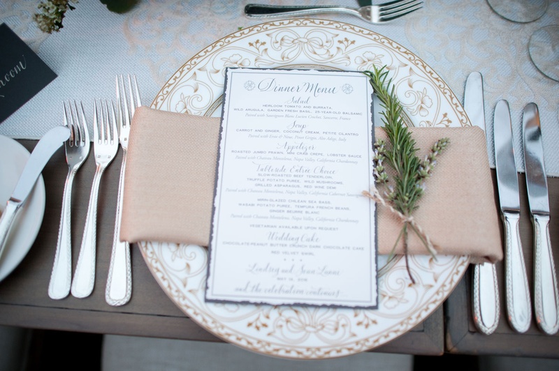 Ornate Charger with Champagne Napkin
Photography: Triple Cord Photography
Read More:
http://www.insideweddings.com/weddings/destination-wedding-with-outdoor-reception-lavish-after-party/982/ White plate with ornate design and blue menu card calligraphy greenery twine runner