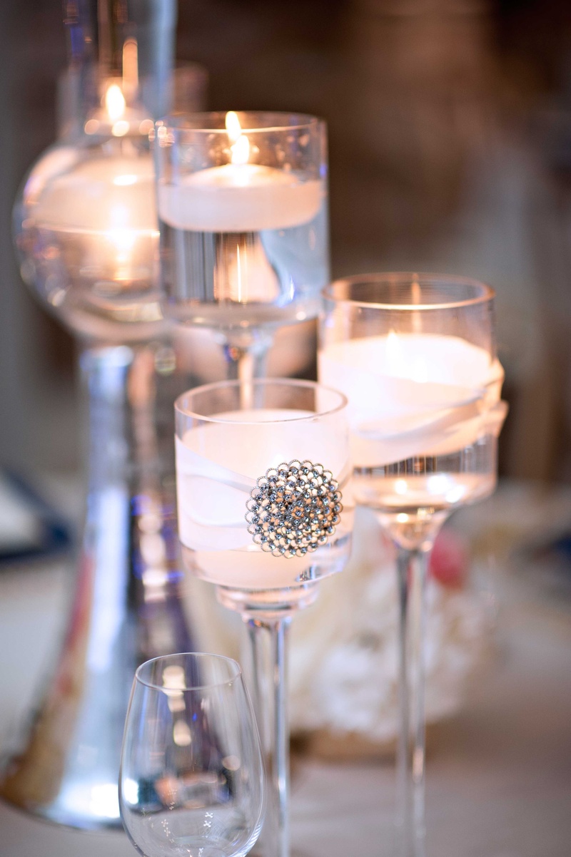 Floating Candles in Glass Votives
Photography: Carasco Photography
Read More:
http://www.insideweddings.com/weddings/church-ceremony-with-nigerian-traditions-chic-ballroom-reception/845/ Floating candles in wedding centerpiece tall glass votives with ribbon and jewel decal