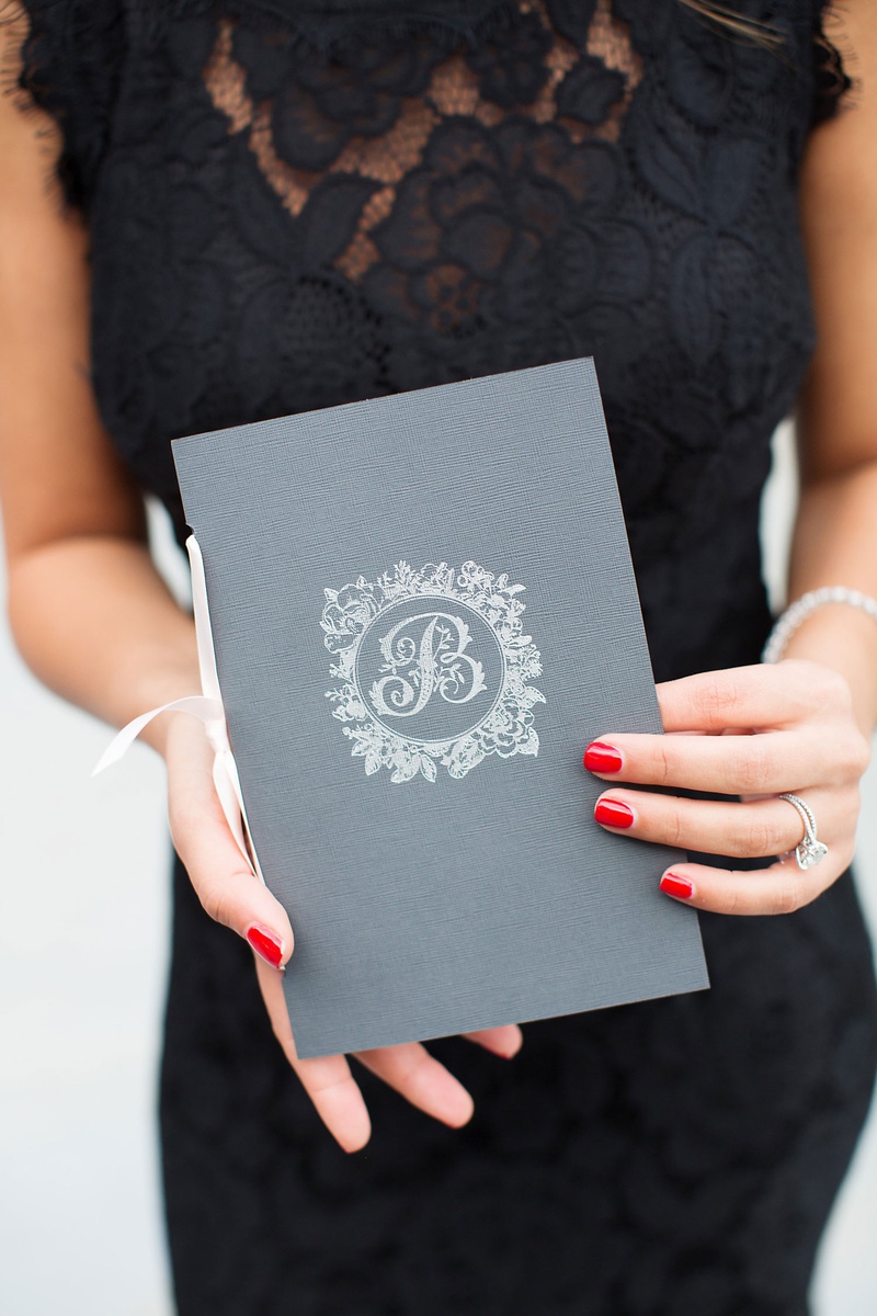 Grey Ceremony Program with White Monogram
Photography: Sarah Kate, Photographer
Read More:
http://www.insideweddings.com/weddings/outdoor-fall-ceremony-opulent-tented-reception-in-dallas-texas/1022/ Wedding ceremony program being held by woman in black lace dress red manicure pink ribbon