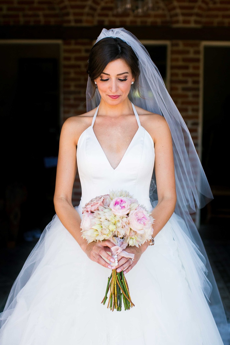 Bride in Halter Ball Gown with Blush %26 White Bouquet
Photography: Callaway Gable
Read More:
http://www.insideweddings.com/weddings/alfresco-summer-wedding-with-lush-foliage-accents-in-california/805/ bride in white tulle ball gown with plunging halter neckline looking down at blush ivory bouquet