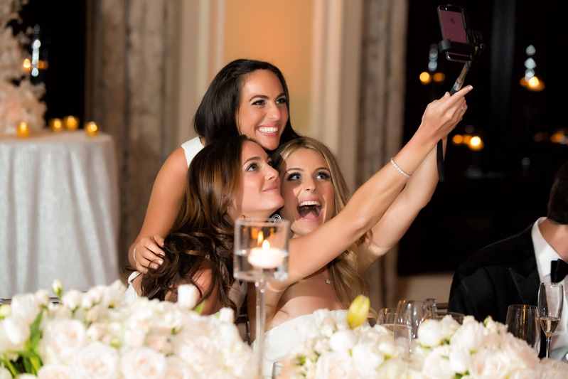 Bride Taking Selfie with Bridesmaids
Photography: Muñoz Photography
Read More:
http://www.insideweddings.com/weddings/colorful-jewish-ceremony-ballroom-reception-at-the-breakers/818/ Bride sitting down at reception taking selfie with bridesmaids on selfie stick