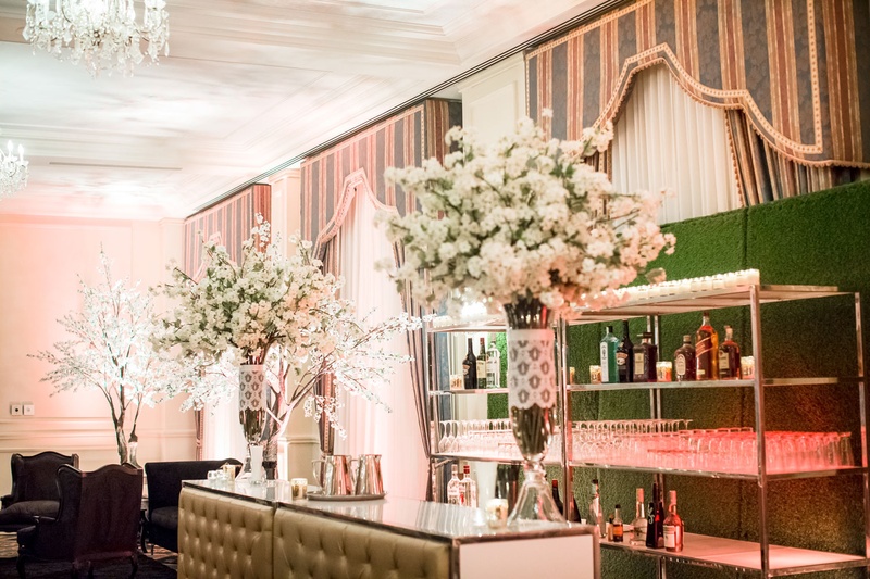 Wedding Bar with Tall White Flowers
Photography: Magnolia Studio
Read More:
http://www.insideweddings.com/weddings/charming-church-ceremony-romantic-ballroom-reception-in-quebec/1075/ Tufted bar with glasses and bottles on shelf in front of hedge wall greenery lace around glass vases