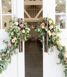 Decorated Doors to Reception Space
Photography: Braedon Photography
Read More:
http://www.insideweddings.com/weddings/colorful-wedding-featuring-a-punchy-peach-palette/1173/ Large white barn farmhouse doors decorated with greenery pink rose yellow rose orange rose flowers