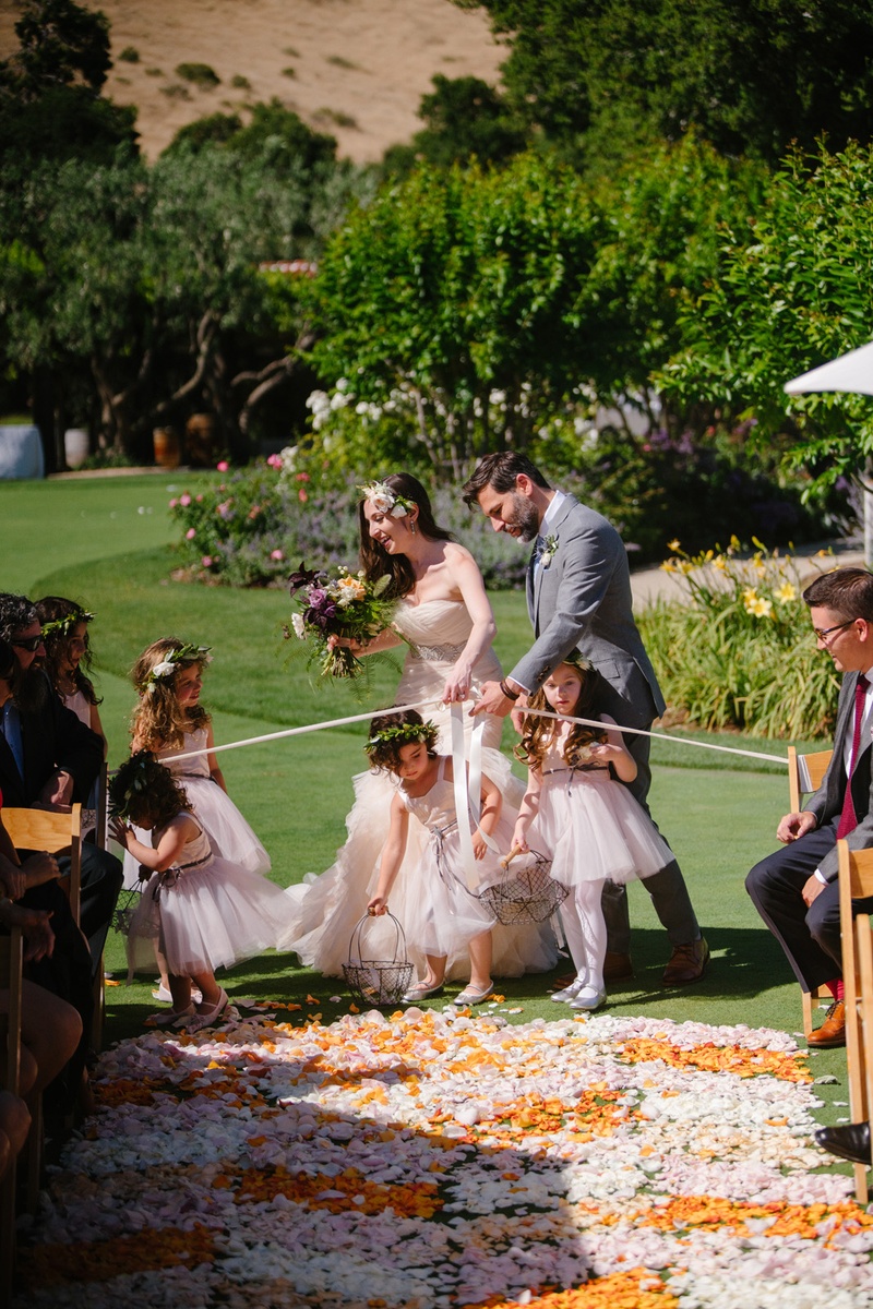 Bride and Groom Help Flower Girls
Photography: Karlisch Photography
Read More:
http://www.insideweddings.com/weddings/modern-rustic-wedding-full-of-flowers-and-geometric-details/906/ bride and groom help flower girls into aisle blocked with ribbon
