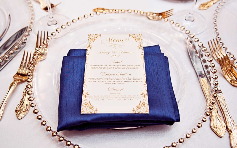 Blue %26 Gold Place Setting
Photography: Carasco Photography
Read More:
http://www.insideweddings.com/weddings/church-ceremony-with-nigerian-traditions-chic-ballroom-reception/845/ White tablecloth, gold flatware, gold menu card, navy blue dinner napkin, gold beaded charger plate