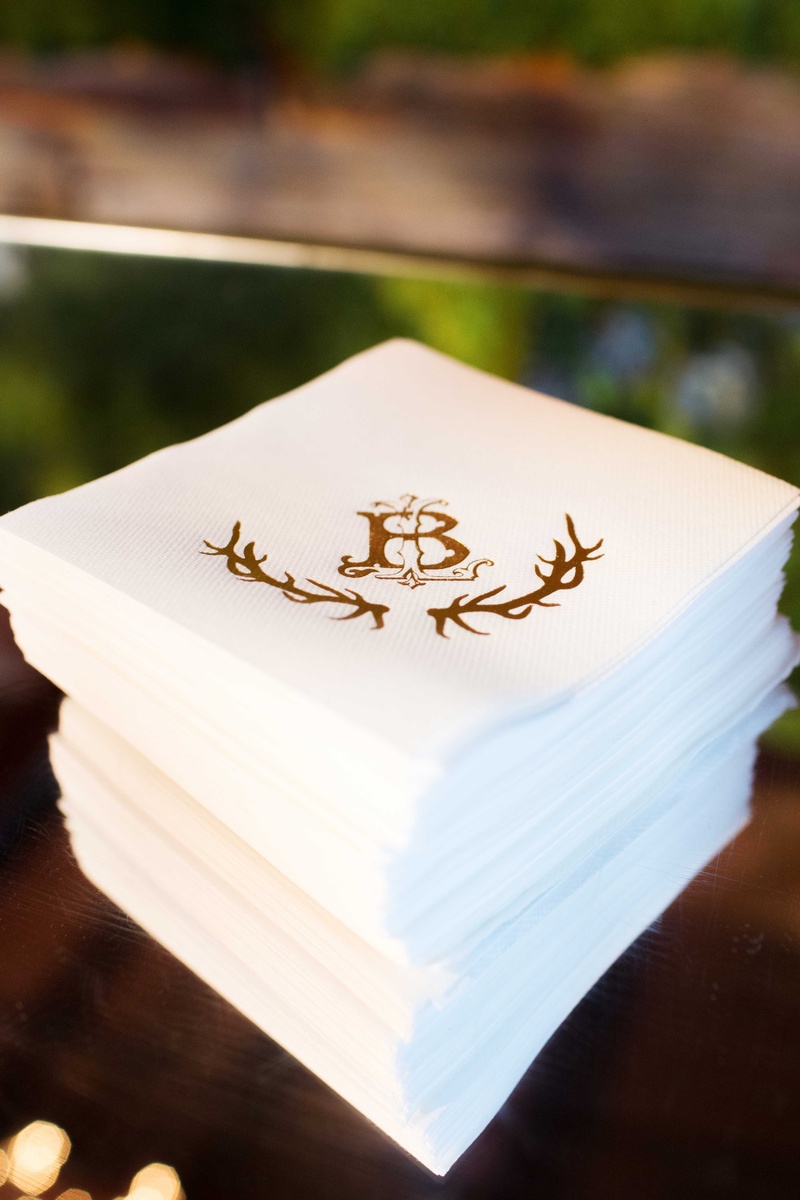Cocktail Napkins with Antler Motif
Photography: Perez Photography
Read More:
http://www.insideweddings.com/weddings/incredible-tented-ceremony-barn-reception-at-ranch-in-aspen/860/ Stack of white cocktail napkins with gold wedding monogram and antler design