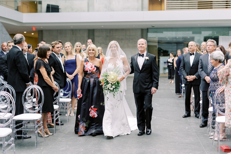 Bride with Parents at Museum Wedding
Photography: Lauren Gabrielle Photography
Read More:
http://www.insideweddings.com/weddings/summer-real-wedding-featuring-tropical-decor-at-an-art-museum/1328/ bride with veil over face walking down aisle with mother in flower print one shoulder gown father