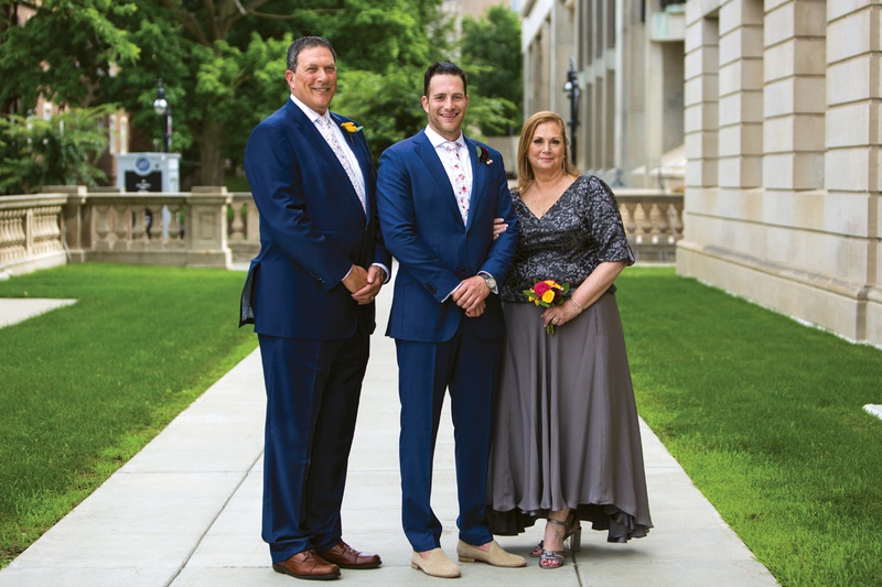 Groom with His Parents Before Wedding
Photography: Kent Drake Photography
Read More:
http://www.insideweddings.com/weddings/bright-and-colorful-wedding-palette-with-ceremony-overlooking-lake/1315/ groom on sidewalk standing in between his father in navy suit, mother in grey dress & small nosegay