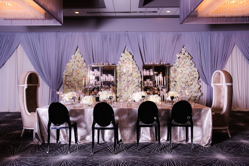 Grand Head Table at Styled Shoot
Photography: Gold Grid Studios
Read More:
http://www.insideweddings.com/weddings/celebratory-wedding-shoot-with-elegant-romantic-decor-in-chicago/728/ Wedding reception with long head table in silver tablecloth, black ghost chairs, floral panels