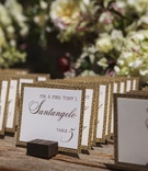 Escort Cards with a Rustic Touch
Photography: Mischa Photography
Read More:
http://www.insideweddings.com/weddings/heartwarming-ranch-wedding-with-sophisticated-rustic-details/673/ Outdoor ranch wedding reception with place cards with burlap print edges propped on tiny wood blocks