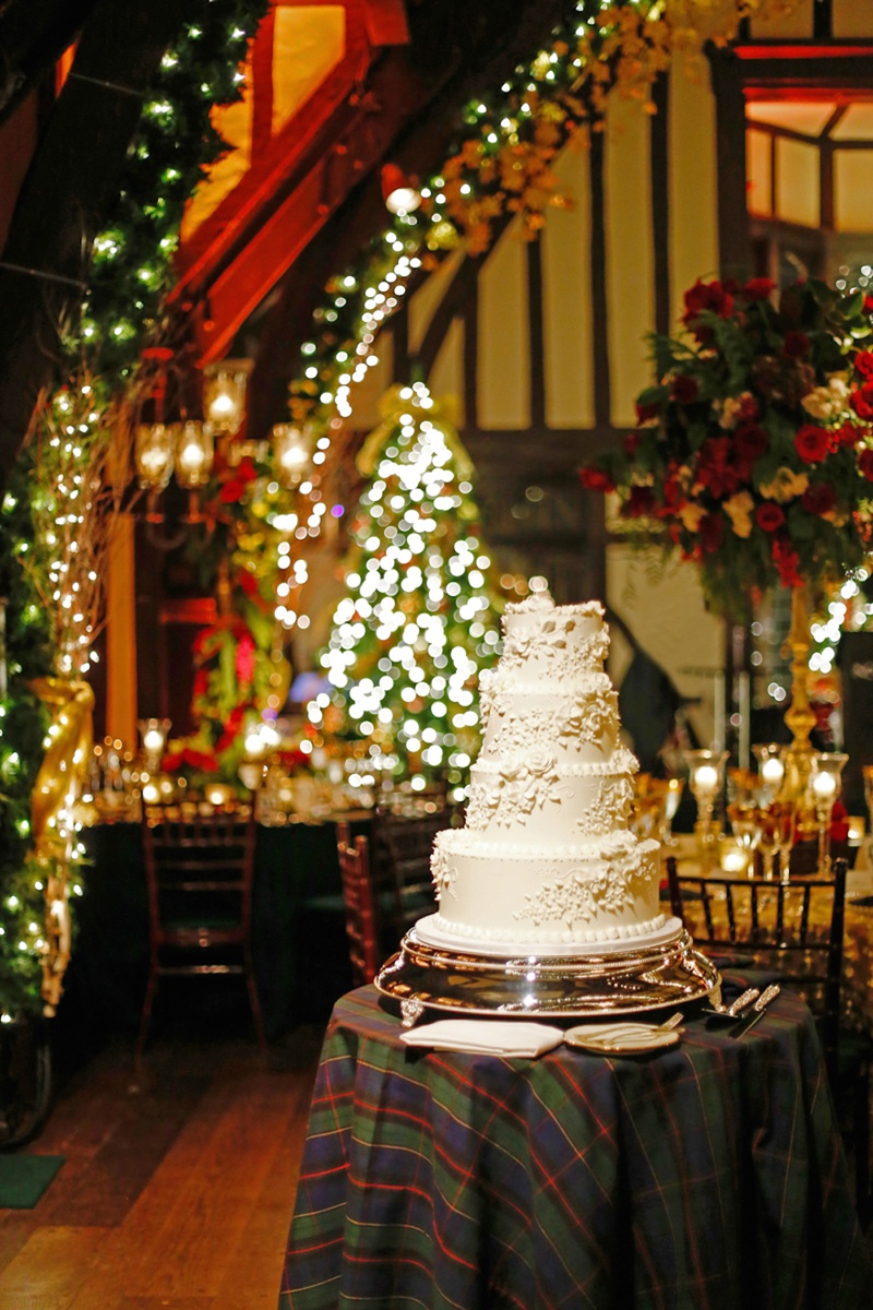 Traditional Wedding Cake at Holiday Wedding
Photography: Robyn Rachel Photography
Read More:
http://www.insideweddings.com/weddings/christmas-theme-wedding-with-festive-red-green-decor-in-illinois/729/ Four layer white wedding cake on plaid cake table in reception room filled with Christmas decoration
