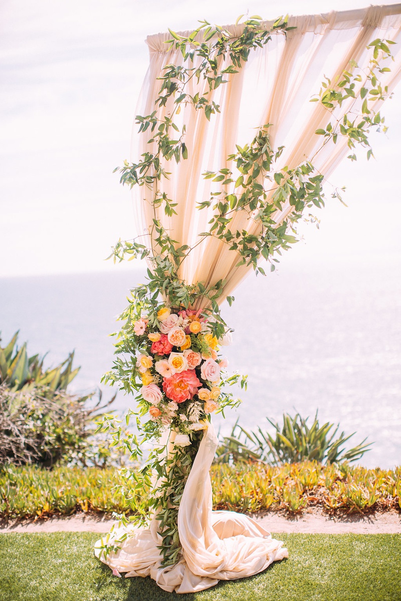 Drapery Arch Decorated with Greenery
Photography: Ashley Paige Photography
Read More:
http://www.insideweddings.com/weddings/romantic-ocean-view-ceremony-charming-reception-in-california/1337/ wedding ceremony overlooking ocean drapery arch pink orange yellow flowers