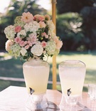 Lemonade in Drink Dispensers at Ceremony
Photography: Patrick Moyer
Read More:
http://www.insideweddings.com/weddings/vintage-inspired-alfresco-ceremony-fairy-tale-ballroom-reception/1030/ Outdoor wedding ceremony flower arrangement on wood table with drink dispensers filled with lemonade