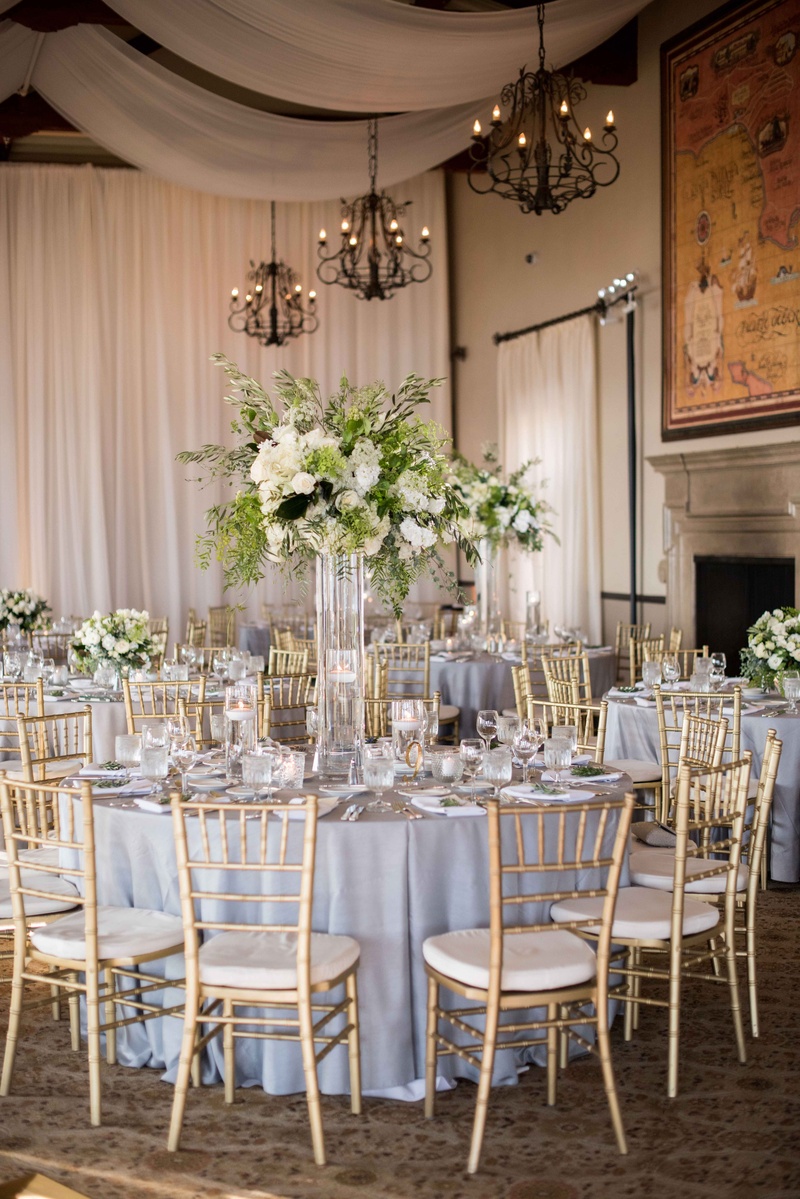 Tall Centerpieces with White Blooms and Verdure
Photography: Laurie Bailey Photography
Read More:
http://www.insideweddings.com/weddings/classic-california-wedding-with-outdoor-ceremony-indoor-reception/853/ gold chiavari chairs, lucite vessel holding green and white flower arrangement