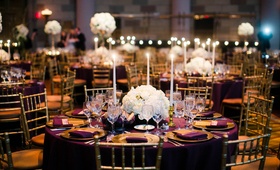 Low White Hydrangea Centerpiece at Round Table
Photography: Images by Berit, Inc.
Read More:
http://www.insideweddings.com/weddings/gatsby-inspired-jewish-wedding-with-purple-gold-decor-in-new-york/720/ Round wedding reception table with purple linen, gold plates, tall candles, and white flowers