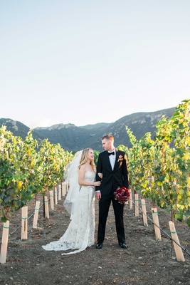 Valentines Day At California Vineyard Bride In Jim Hjelm Wedding Dress And Groom Stand In Vineyard Vines California Red Bouquet Of Valentines Day At California Vineyard Bride In Jim Hjelm Wedding Dress And Groom Stand In Vineyard Vines California Red Bouquet Of