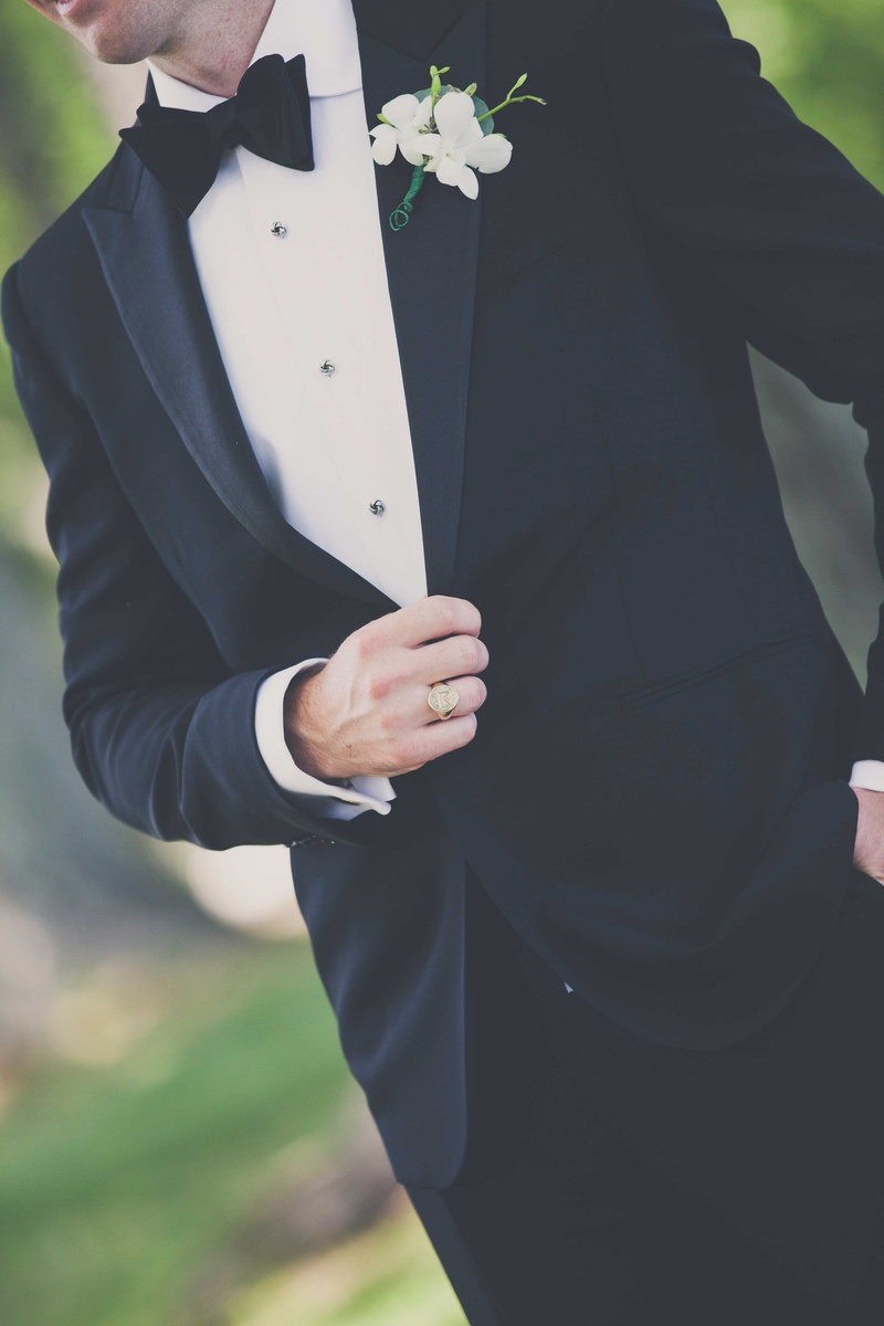 Groom's Tuxedo and White Boutonniere
Photography: Michael Bambino %26 Co.
Read More:
http://www.insideweddings.com/weddings/whimsical-open-air-secret-garden-wedding-with-soft-spring-hues/777/ a close up shot of a grooms black tuxedo and his white and green boutonneire