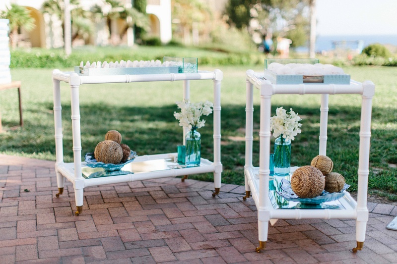 Bar Cart Escort Card Display
Photography: Braedon Photography
Read More:
http://www.insideweddings.com/weddings/orthodox-jewish-wedding-with-outdoor-ceremony-inspired-by-the-sea/812/ White bar carts outside with seashell escort place cards in blue trays with rope circle decor