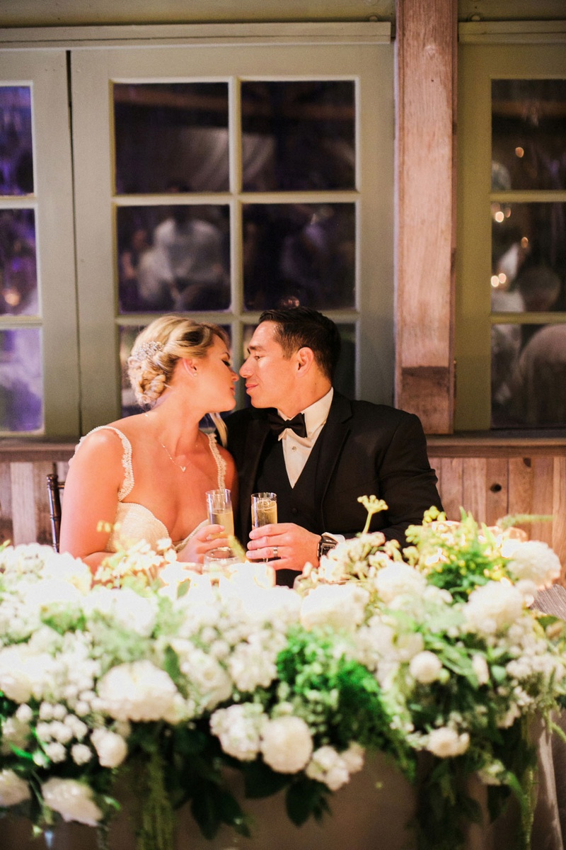 Newlyweds About to Kiss at Sweetheart Table
Photography: This Modern Romance
Read More:
http://www.insideweddings.com/weddings/rustic-chic-wedding-with-wooden-accents-and-verdant-details/861/ bride in galia lahav groom in men's wearhouse about to kiss sweetheart table wedding toasts
