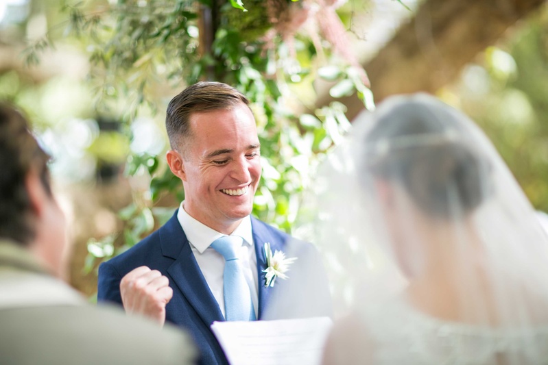 Groom Smiles During Outdoor Ceremony
Photography: Samuel Lippke Studios
Read More:
http://www.insideweddings.com/weddings/a-rustic-camp-themed-outdoor-wedding/908/ Groom in navy blue suit and light blue tie smiles and fist pumps yes gesture during wedding ceremony