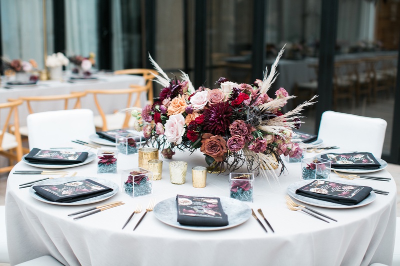 Edgy Centerpiece with Roses and Pampas Grass
Photography: Jessica Claire Photography
Read More:
http://www.insideweddings.com/weddings/unique-chic-bridal-shower-with-dark-and-moody-color-scheme/1335/ round table with centerpiece of burgundy and mauve roses with pampas grass