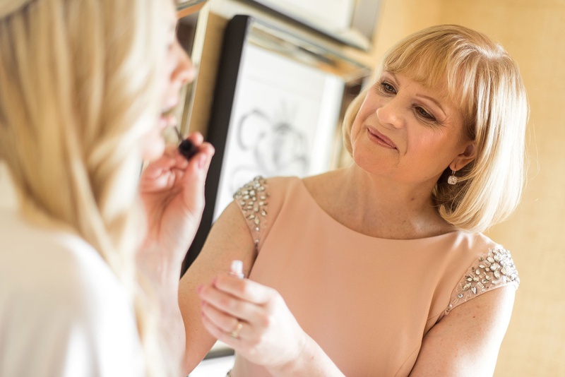 Mother of Bride Helping with Makeup
Photography: Suzanne Delawar Studios
Read More:
http://www.insideweddings.com/weddings/intimate-oceanfront-wedding-with-romantic-red-pink-white-palette/1235/ bride in white robe getting lip gloss put on by mother of bride in peach dress crystal shoulder