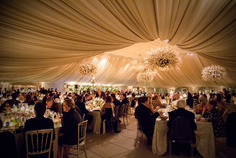 Guests Seated in Dramatic Reception Space
Photography: Carasco Photography
Read More:
http://www.insideweddings.com/weddings/traditional-ceremony-glamorous-garden-inspired-tented-reception/943/ Guests enjoying dinner at wedding reception in heavily draped ballroom with flower chandeliers