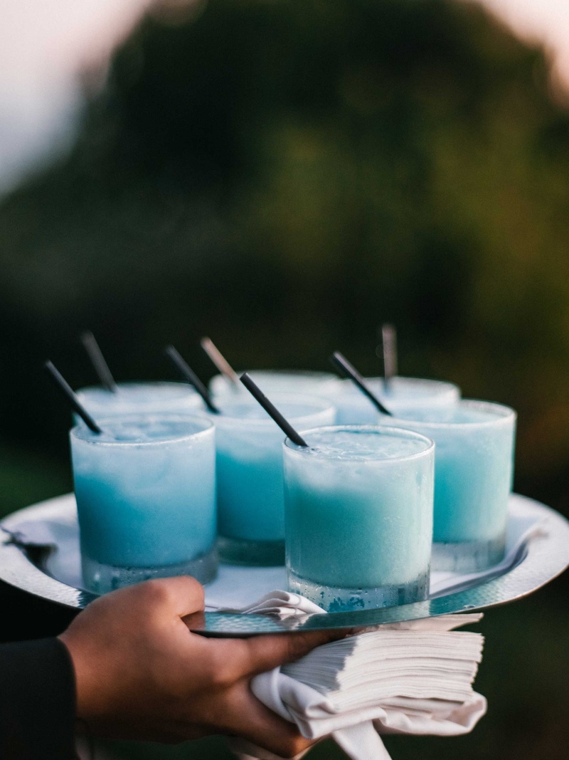 Sky Blue Signature Cocktail
Photography: Braedon Photography
Read More:
http://www.insideweddings.com/weddings/orthodox-jewish-wedding-with-outdoor-ceremony-inspired-by-the-sea/812/ Rocks glass filled with light blue frozen cocktail on silver tray held by server black straws