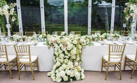 Head Table with Draping Arrangement
Photography: Robert Evans Studios
Read More:
http://www.insideweddings.com/weddings/traditional-catholic-ceremony-romantic-tented-at-home-reception/664/ Wedding reception in a glass tent structure head table with large arrangement of white hydrangeas