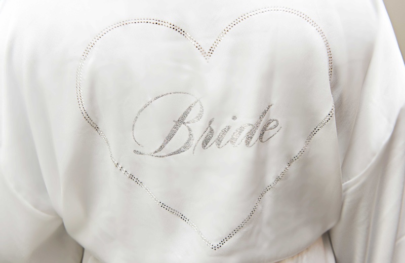 Silver Bride Embroidery on Robe
Photography: Carasco Photography
Read More:
http://www.insideweddings.com/weddings/church-ceremony-with-nigerian-traditions-chic-ballroom-reception/845/ White silky robe with silver heart and bride written on inside bride robe