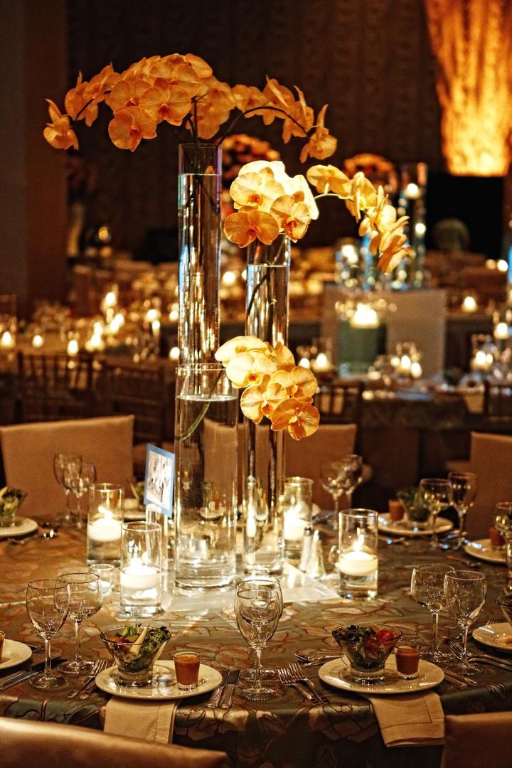 Centerpieces
Photography: Tomas Ramos Photographers
Read More:
http://www.insideweddings.com/weddings/houston-indian-wedding-celebration-with-800-person-guest-list/435/ Wedding reception table with three cylinder vases with orchid stems surrounded by candles
