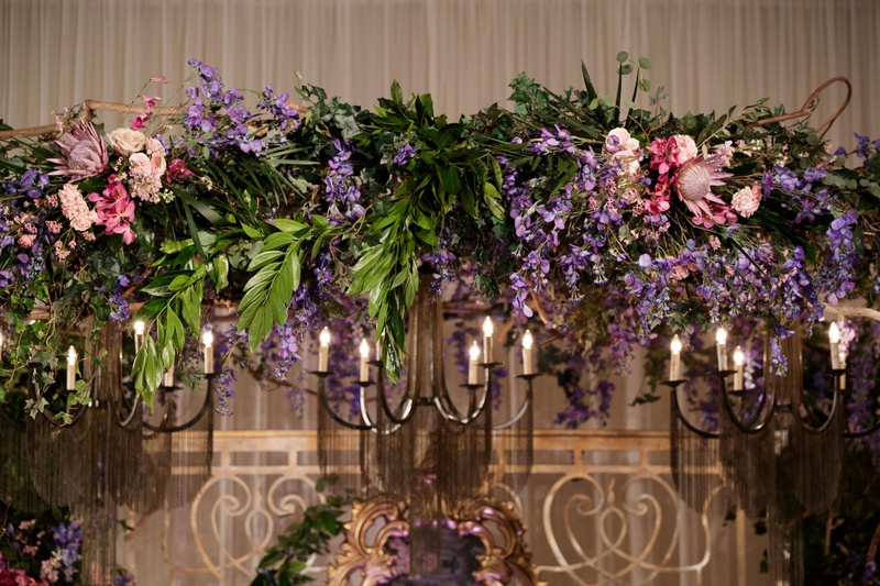Purple Flowers and Iron Light Fixture
Photography: Bob %26 Dawn Davis Photography
Read More:
http://www.insideweddings.com/weddings/inspiring-styled-shoot-with-deep-dark-color-palette-in-chicago/1037/ ceremony arch with purple and blush flowers, pink protea bloom, greenery, iron light fixture